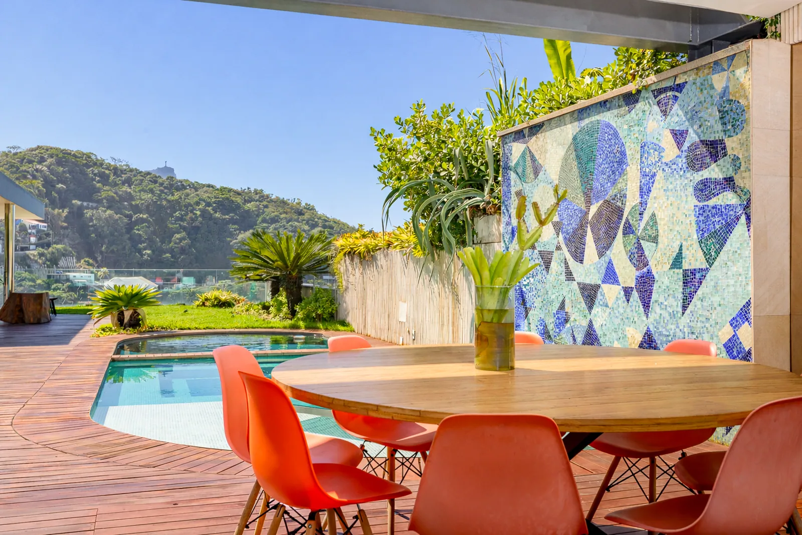 Outdoor dining table facing the pool, mosaic mural behind